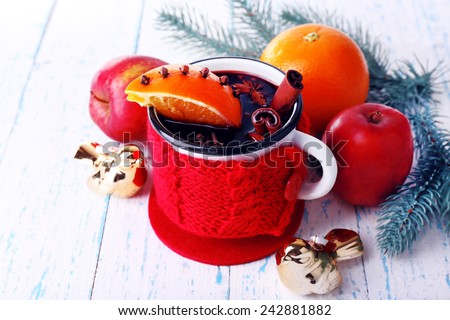 Mug of mulled wine with piece of orange, spice, branch of Christmas tree and other fruits on color wooden background