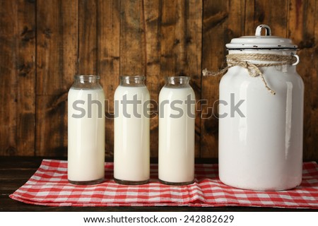 Milk can with glass bottles on napkin on rustic wooden background