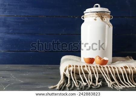 Milk can with eggshell on color wooden background