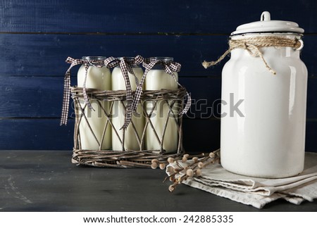 Milk can and glass bottles on color wooden background