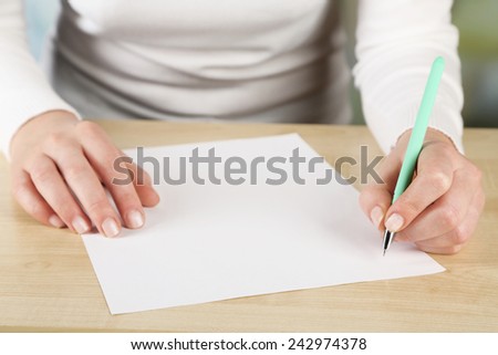 Female hand with pen and sheet of paper at wooden desktop on light background