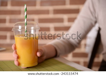 Female sitting at table with fast food closed cup of orange juice on brick wall background