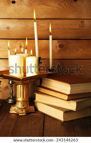 Retro candlesticks with candles and books, on wooden background