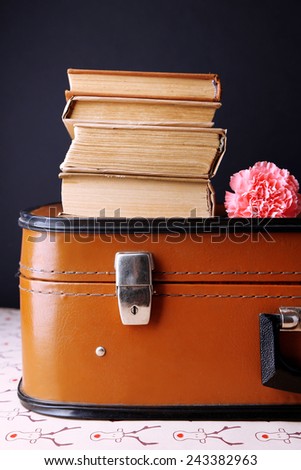 Vintage suitcase with pile on books on patterned surface and dark background