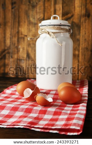 Milk can with eggs and eggshell on napkin on rustic wooden background