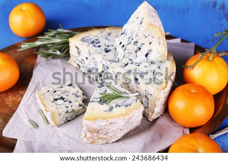 Blue cheese with sprigs of rosemary and oranges on metal tray with sheet of paper and color wooden table background