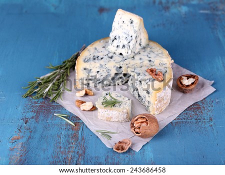 Blue cheese with sprigs of rosemary and nuts on sheet of paper and color wooden table background