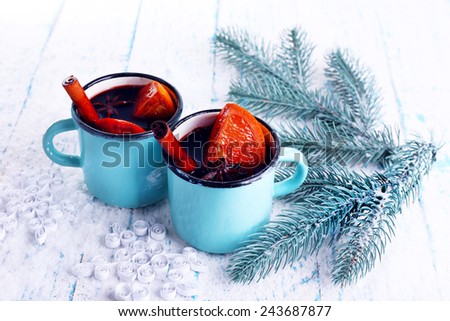 Mugs of mulled wine with piece of orange and spice on color wooden table background