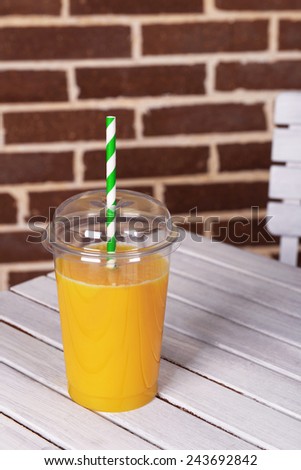 Orange juice in fast food closed cup with tube on wooden table and brick wall background