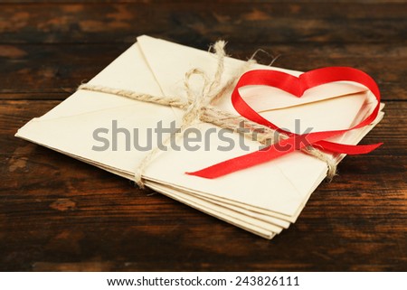 Stack of letters with ribbon in heart shape on rustic wooden table background