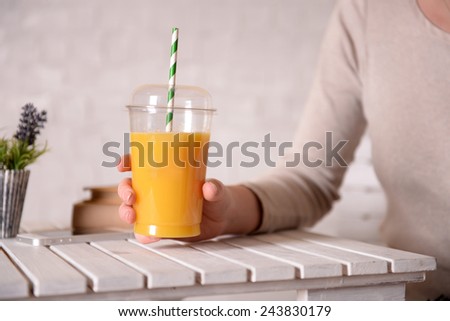 Female hand at wooden table with fast food closed cup of orange juice and near books on light wall background