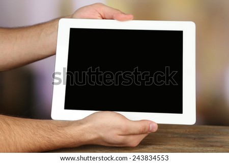 Hands holding tablet PC on wooden table and light blurred background