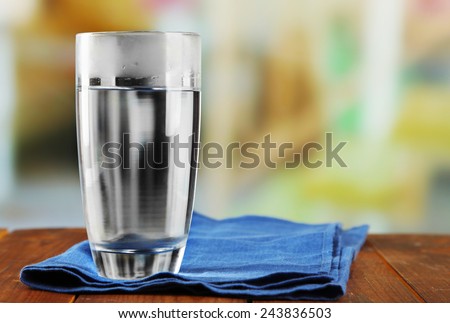 Glass of ice water with napkin on wooden table and light blurred background