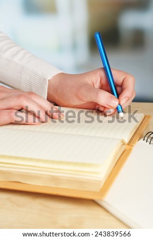 Female hand with pen and diary at wooden desktop on light background