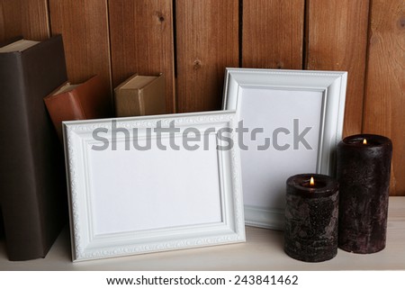 Photo frames with candles and books on wooden surface and wooden wall background