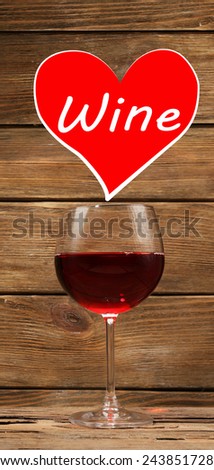 Glass of red wine and sample text in heart on wooden background