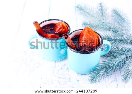Mugs of mulled wine with pieces of orange and spice on snow covered background