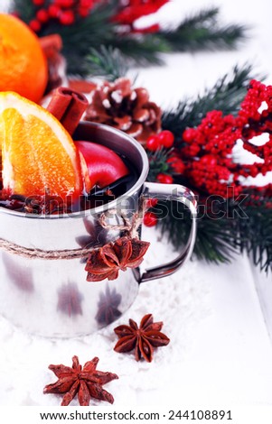 Metal mug of mulled wine with orange and spice and branch of Christmas tree on color wooden background