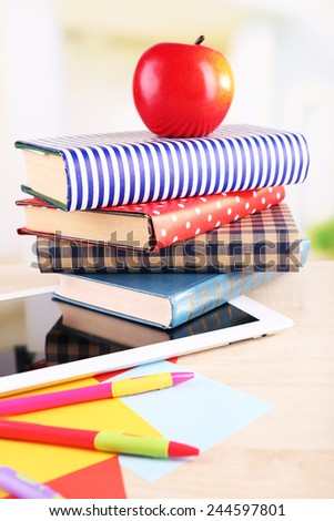 Pile of books with tablet on wooden table and light background