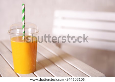Orange juice in fast food closed cup with tube on wooden table and light wall background