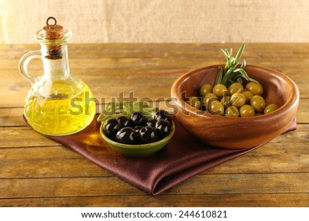 Composition of two round bowls with green and black olives near the oil can on silk cloth, on rustic wooden table, on burlap background