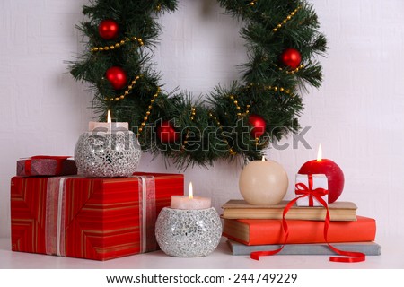 Christmas decoration with wreath, candles and present boxes on shelf on white wall background