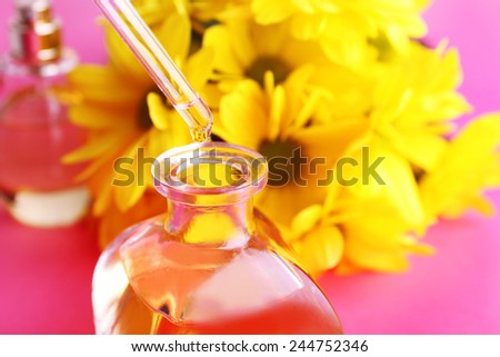 Dropper bottle of perfume with yellow chamomile on pink background