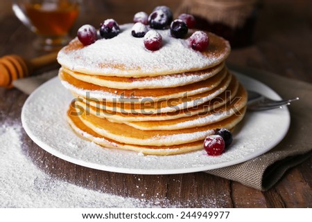 Stack of delicious pancakes with powdered sugar and berries on plate and napkin on wooden background