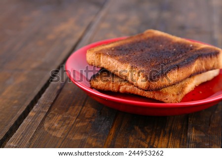 Burnt toast bread on red plate, on wooden table background