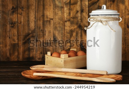 Milk can with eggs and spoons on rustic wooden background