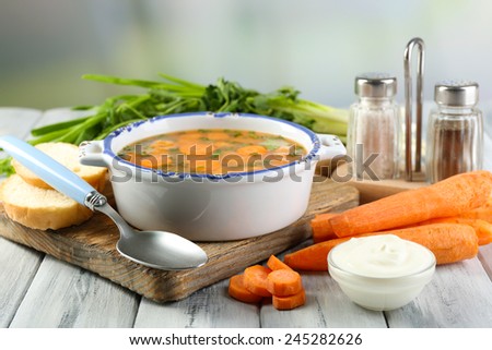Composition with carrot soup, ingredients and herbs on color wooden table, on light background
