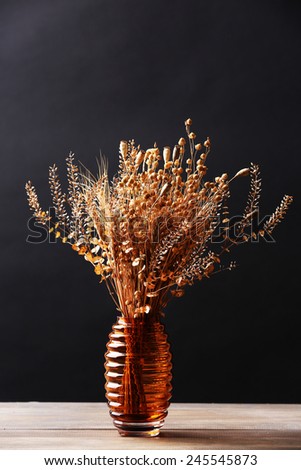 Bouquet of dried flowers in vase on table and dark background