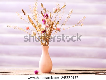 Bouquet of dried flowers in vase on color planks background