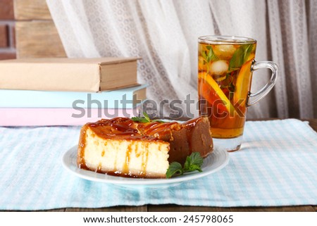 Cheese cake in plate, cup of tea and books on tablecloth on curtain background