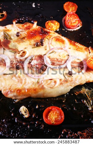 Dish of Pangasius fillet with onion and cherry tomatoes on burn pan background