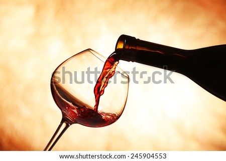 Pouring red wine from bottle into glass on color background