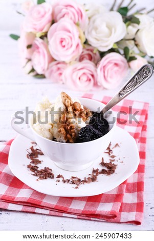 Dessert with prunes in cup with bouquet of roses on color wooden table background