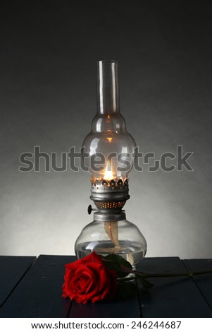 Kerosene lamp with red rose on wooden table on dark lights background