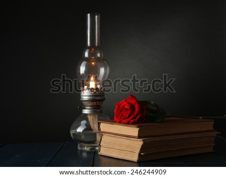 Kerosene lamp with books and red rose on wooden table and dark background