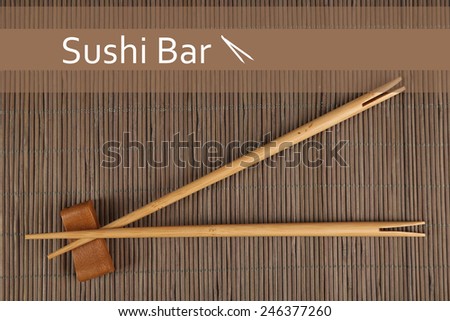 Pair of chopsticks and Sushi Bar text on brown bamboo mat background