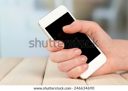 Hand holding smart mobile phone on wooden table and light blurred background