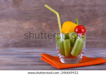Sticks of celery with sweet pepper and cherry tomato in glass with tube and napkin on rustic wooden background