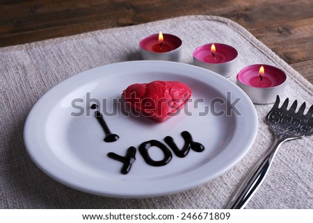 Cookie in form of heart on plate with inscription I Love You, and candles on napkin and wooden table background