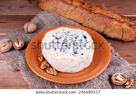 Blue cheese on earthenware dish with nuts and baguette on burlap cloth and wooden table background