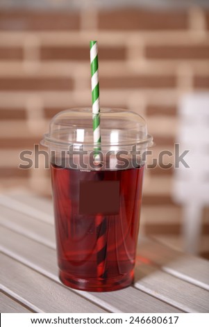 Pomegranate juice in fast food closed cup with tube on wooden table and brick wall background