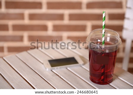 Pomegranate juice in fast food closed cup with tube and mobile phone on wooden table and brick wall background