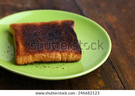 Burnt toast bread on light green plate, on wooden table background