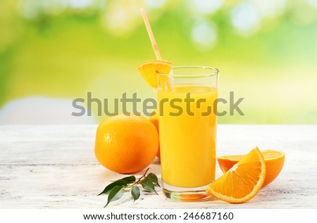 Glass of orange juice with straw and slices on wooden table and bright background