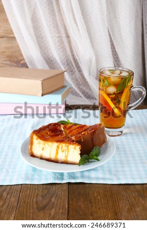 Cheese cake in plate, cup of tea and books on tablecloth on curtain background