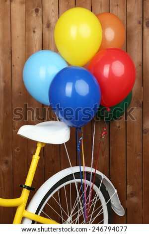 Yellow bicycle with balloons on wooden wall background